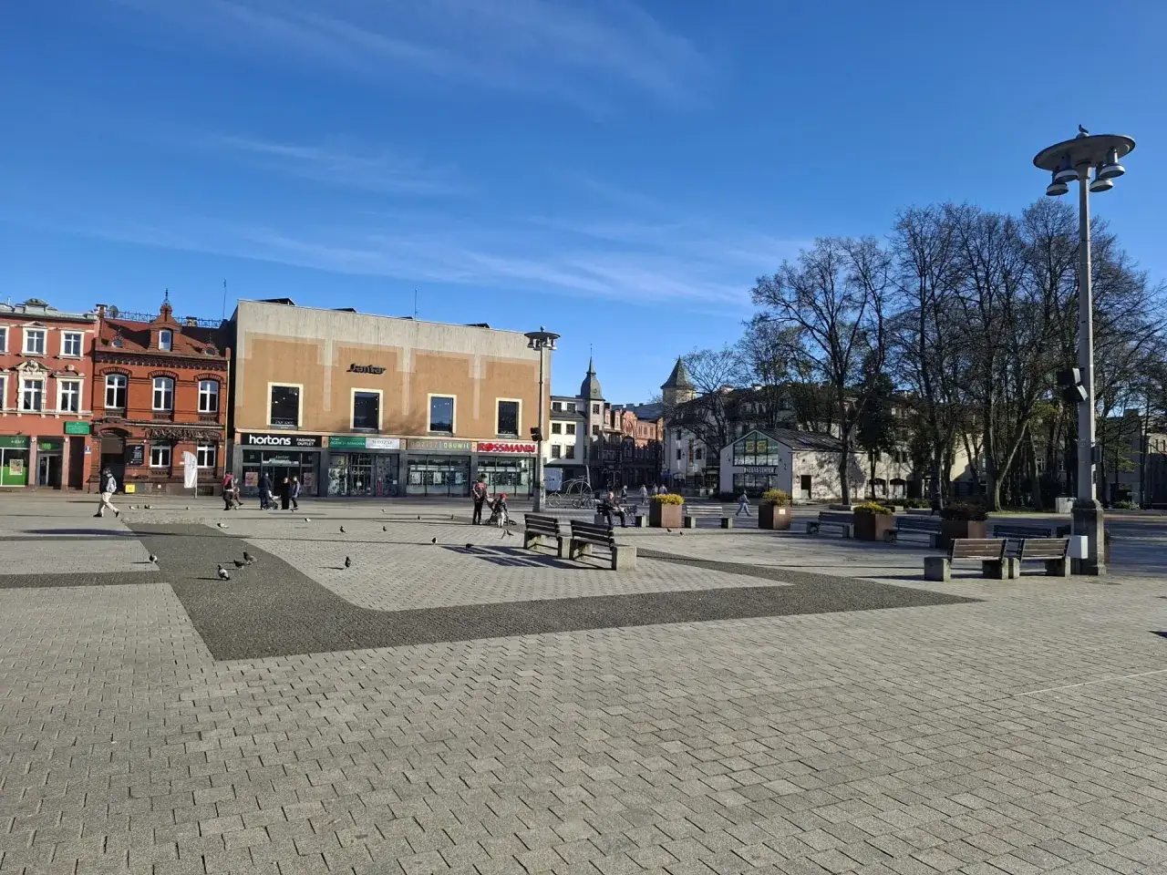 Słoneczny dzień na lęborkim starym mieście. Pustawo na rynku, kilka gołębi spaceruje po bruku.