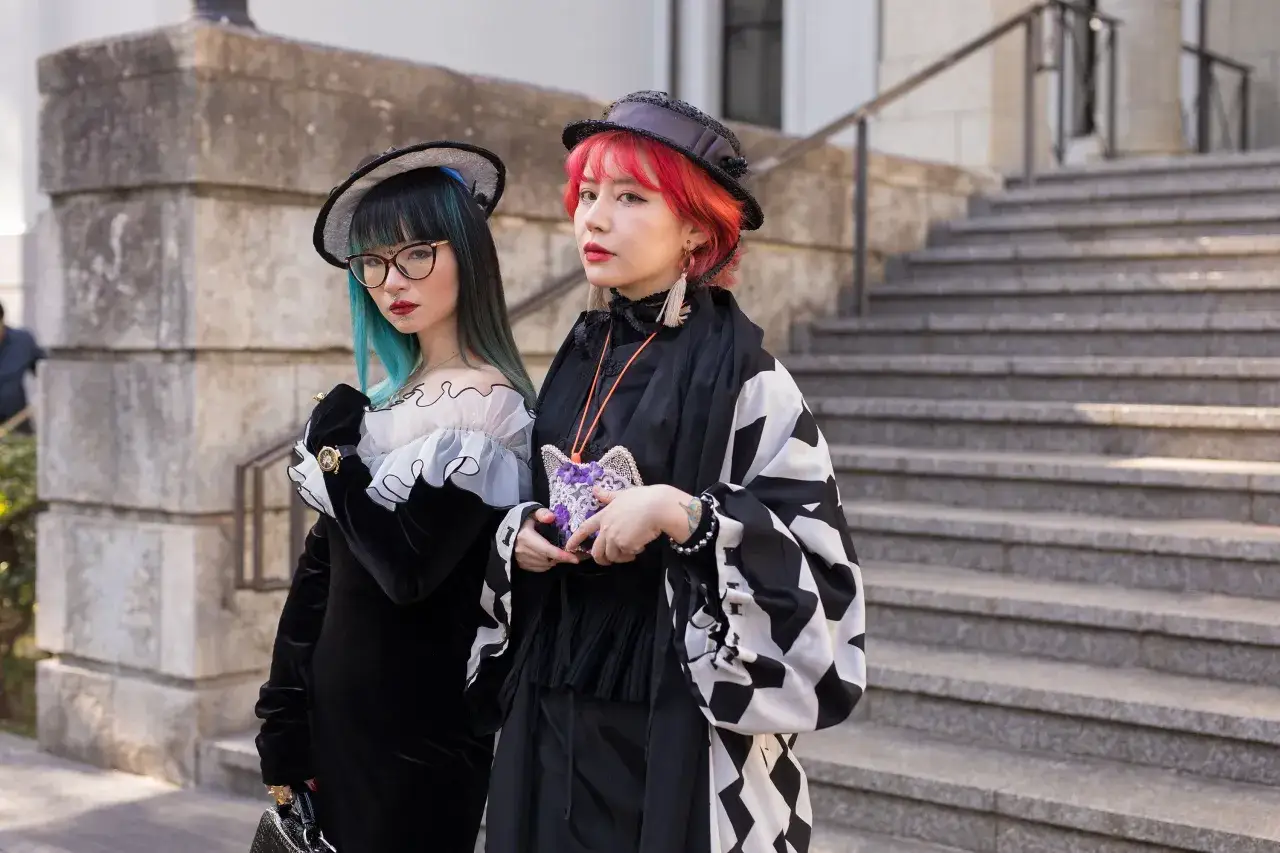 Tv&aring; unga kvinnor med f&auml;rgglatt h&aring;r och unik japan fashion-stil poserar framf&ouml;r en stenbyggnad.