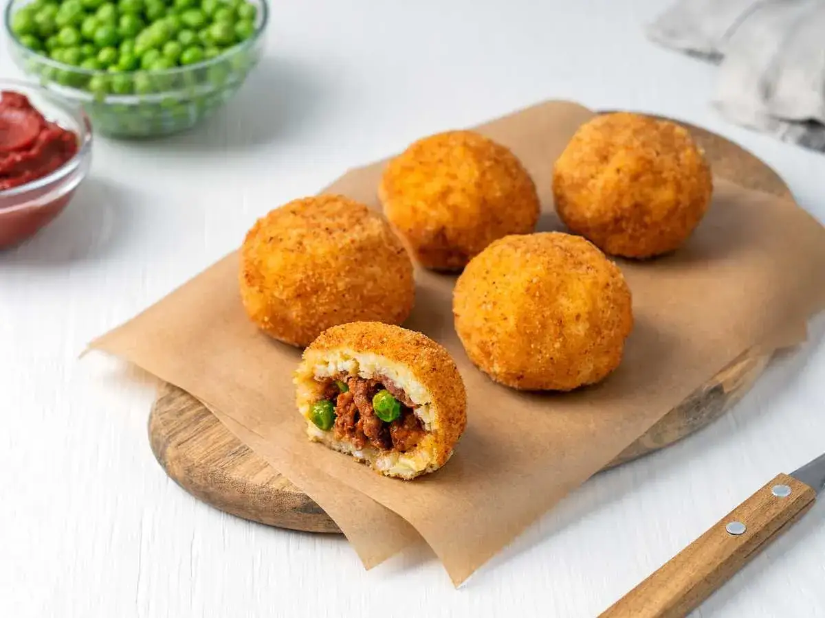 Arancini dorados y crujientes, uno cortado revela un relleno de carne y guisantes. Una deliciosa receta para probar.