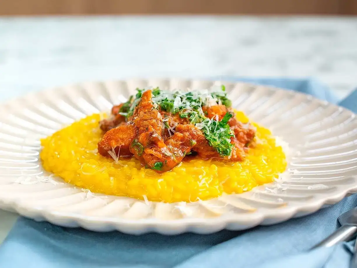En krämig, gul risotto toppas med en mustig gryta av osso buco, garnerad med färsk persilja och riven parmesan.