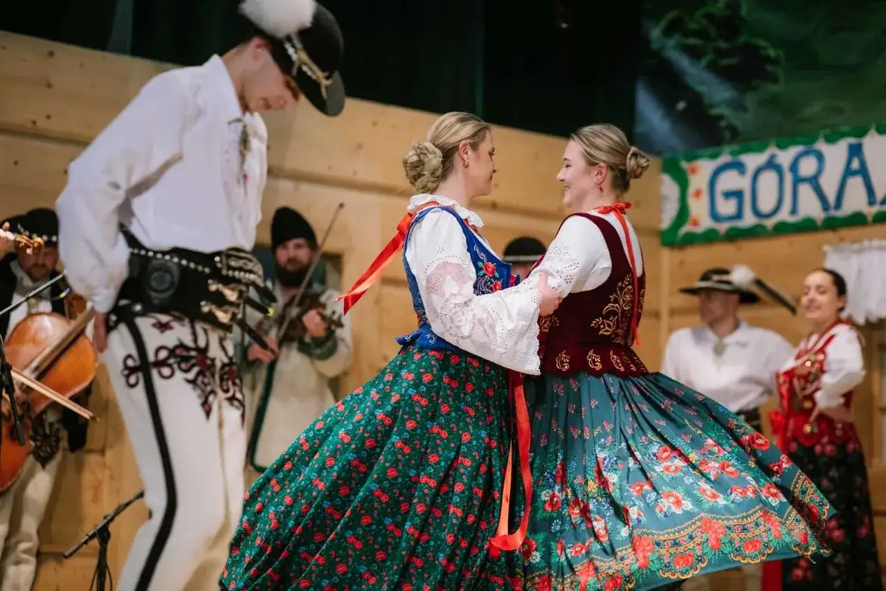 Tancerze w strojach góralskich wirują w rytm muzyki. Góralska muzyka nowoczesną brzmi w tle, gdzie grają skrzypkowie.