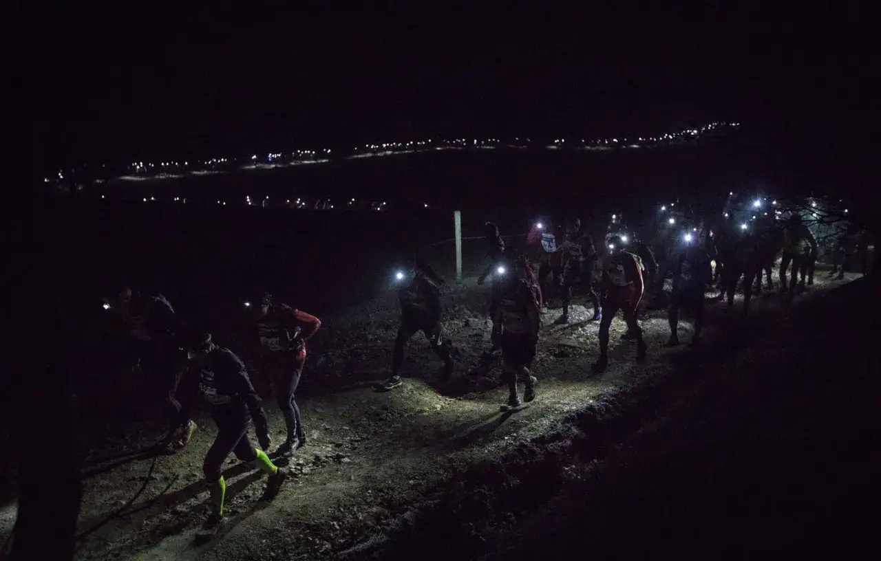Course de trail nocturne, des coureurs illuminent le chemin avec leurs lampes frontales sur le trail Saint-Étienne Lyon.