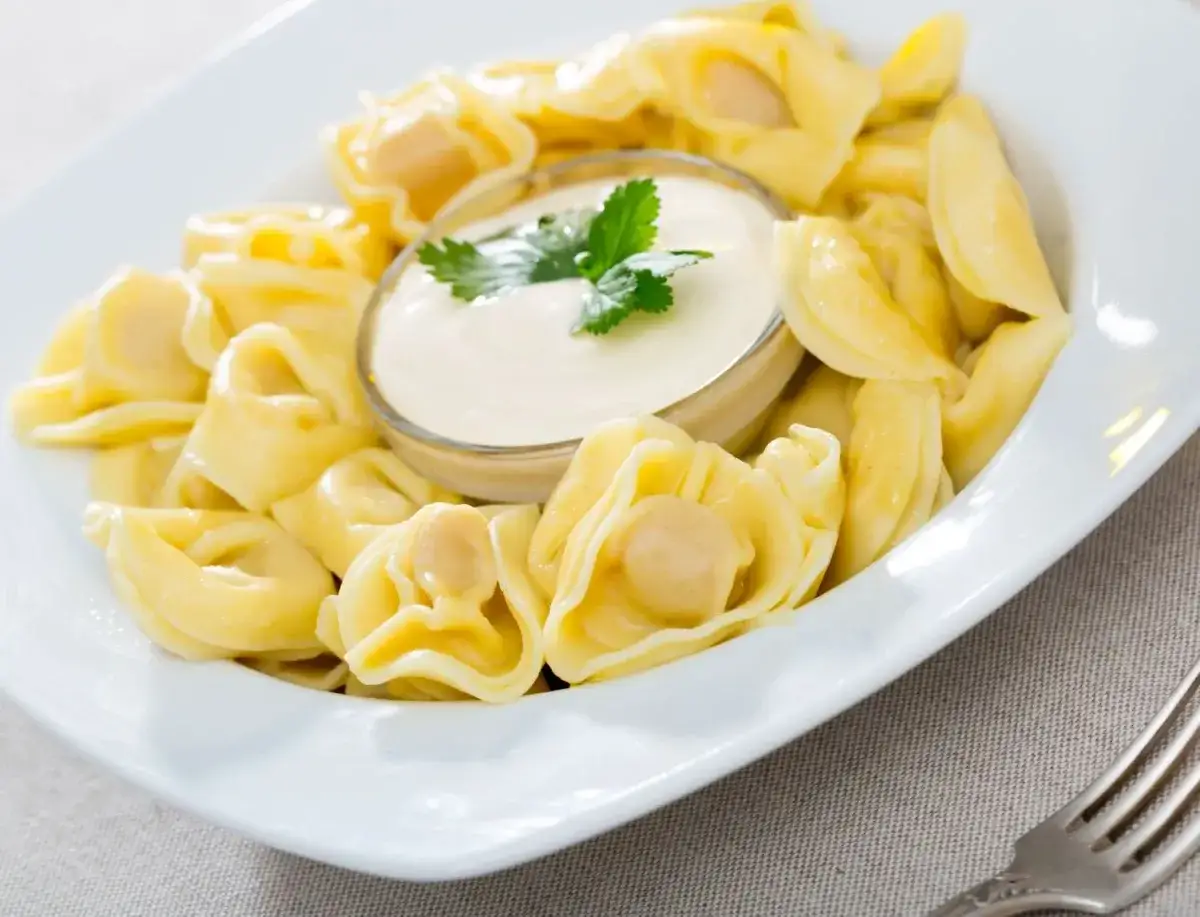 Pyszne pierożki tortellini podane z kremowym, aksamitnym sosem śmietanowym i gałązką natki pietruszki.