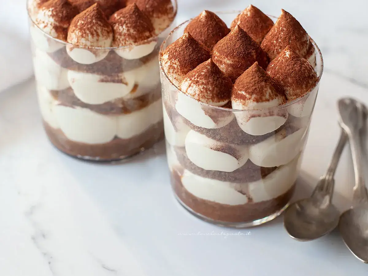 Delizioso tiramisù senza caffè, stratificato con crema e cacao, servito in bicchieri trasparenti.