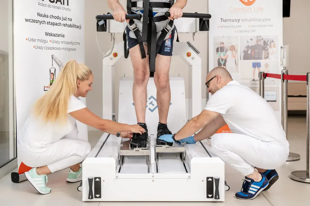 Rehabilitacja po zespoleniu gwoździem gamma. Terapeuci pomagają pacjentowi w specjalistycznym robocie do nauki chodu.