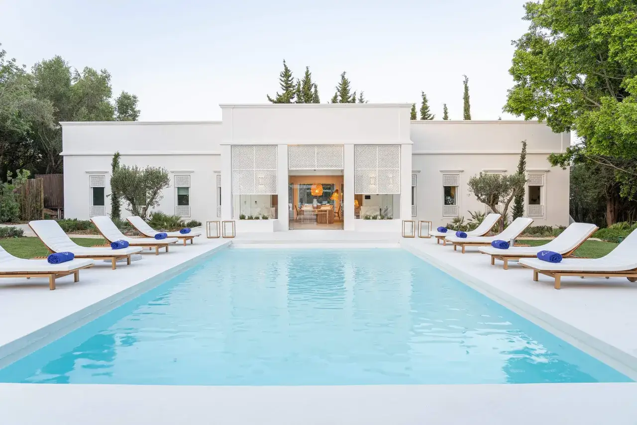 Impresionante villa con piscinas de lujo modernas, tumbonas blancas y toallas azules. Un oasis de tranquilidad y diseño.