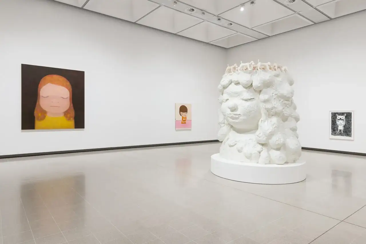 A gallery showcases iconic works by Nara artist, including a large white sculpture of a girl's head adorned with small figures, and two paintings of children.