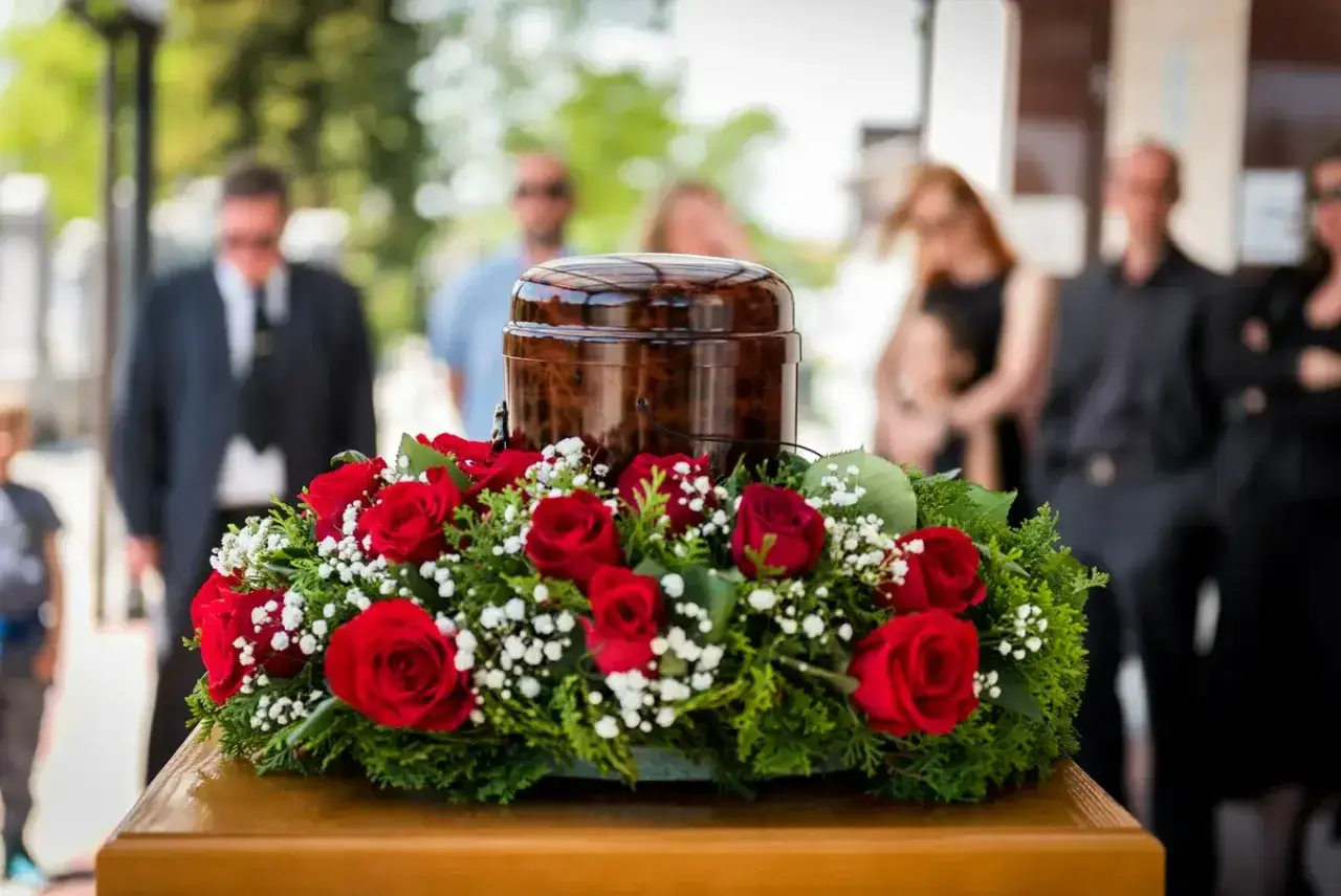 Urzna z czerwonymi różami i ludźmi w tle. To obraz pogrzebu z zasadami, gdzie każdy element ma swoje znaczenie.