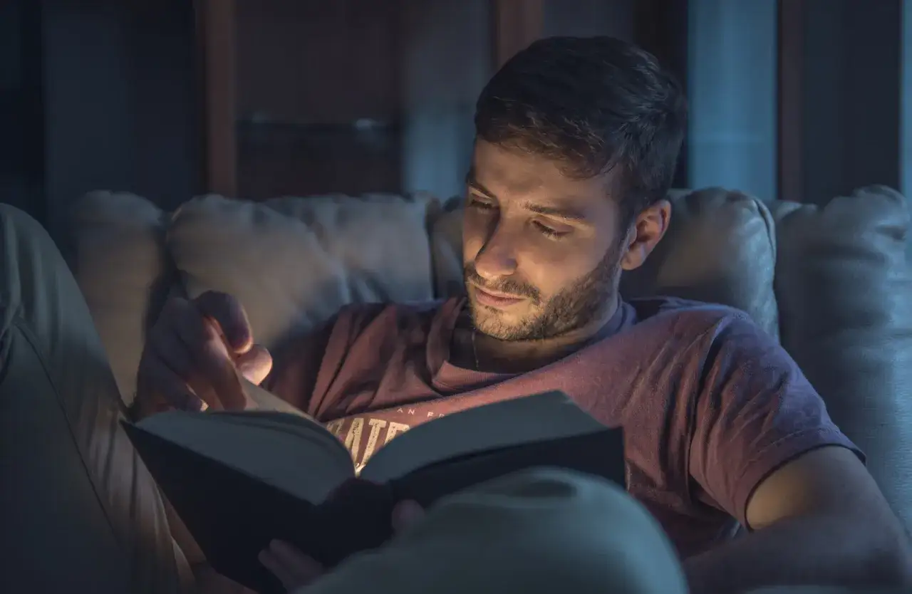 Hombre leyendo un libro con luz tenue, ideal para la vista.