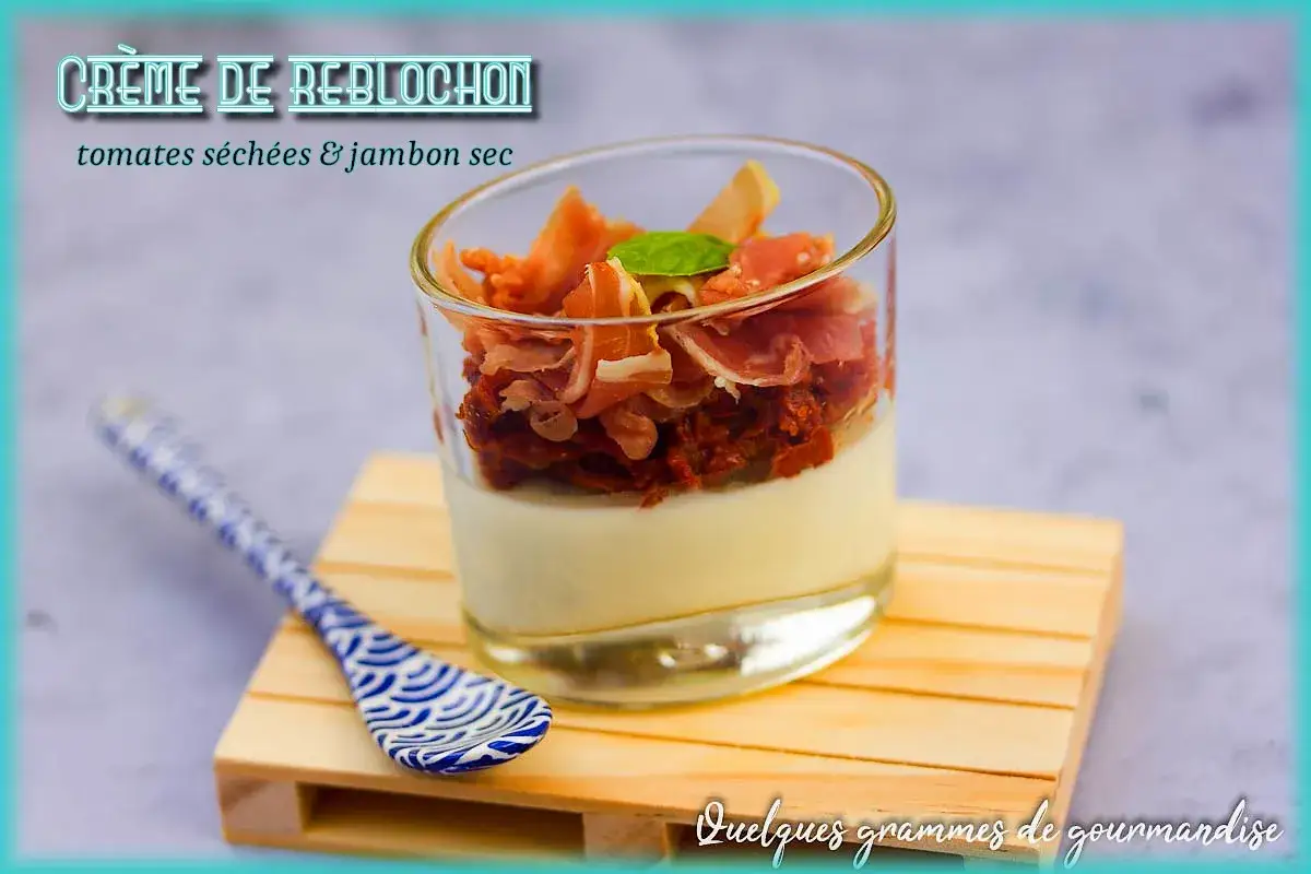 Crème de reblochon on a wooden base, topped with sun-dried tomatoes and prosciutto. A decorative spoon rests beside it.