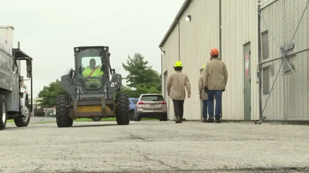 Operario en cargadora frontal, parte del transporte de materiales. Dos trabajadores con cascos observan.