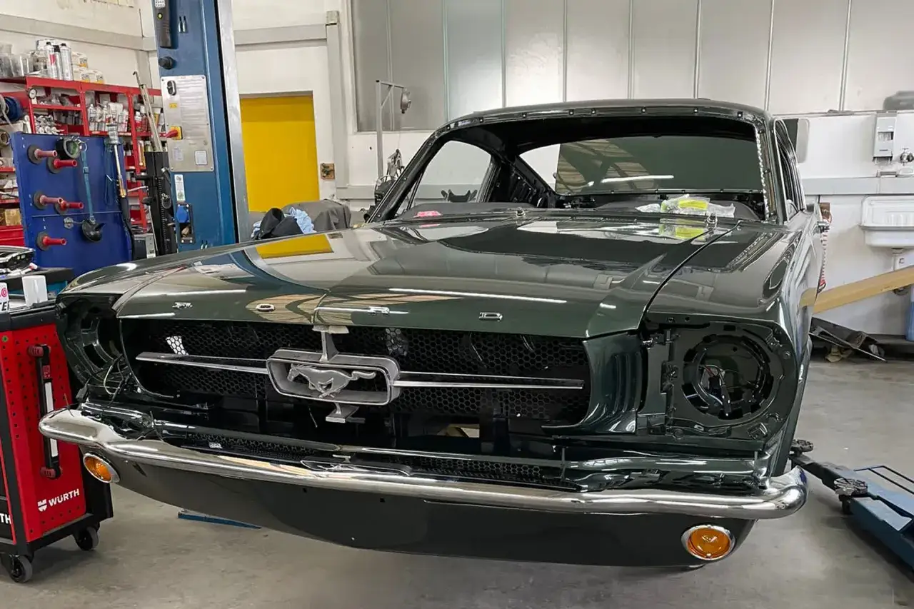 Dunkelgr&uuml;ner Oldtimer, ein Ford Mustang, in der Werkstatt. Die Scheinwerfer fehlen, was auf eine laufende oldtimer restauration kosten hinweist.
