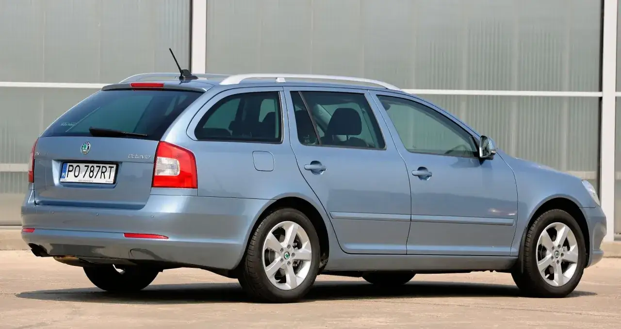 Błękitna Skoda Octavia 2010 kombi z polskimi tablicami PO 787RT stoi na tle nowoczesnego budynku.