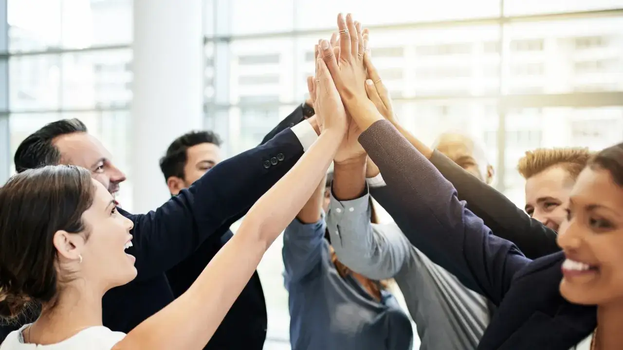 Un grupo diverso de profesionales celebra un &eacute;xito, uniendo sus manos en un gesto de unidad. Son la viva imagen de **high performance teams**.