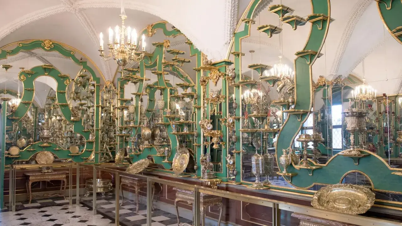 Prunkvolle Schatzkammer Dresden mit unzähligen goldenen Objekten auf grünen Regalen, Spiegeln und Kronleuchtern.