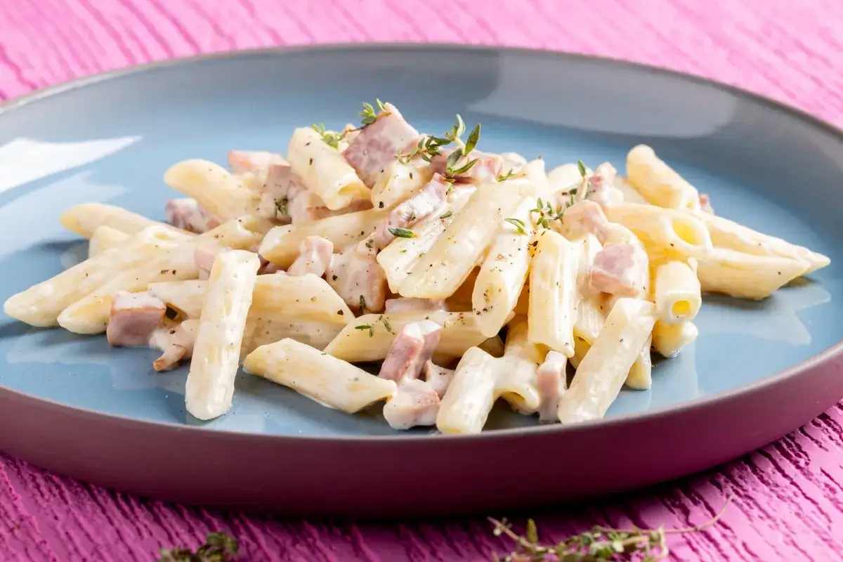 Penne cremose con prosciutto e un tocco di Philadelphia, guarnite con timo fresco. Un piatto semplice e gustoso.