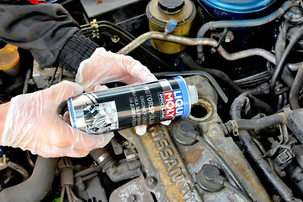 Ręce w rękawiczkach trzymają puszkę z płukanką do silnika Liqui Moly. To dobra płukanka do silnika, która pomoże oczyścić jednostkę napędową.