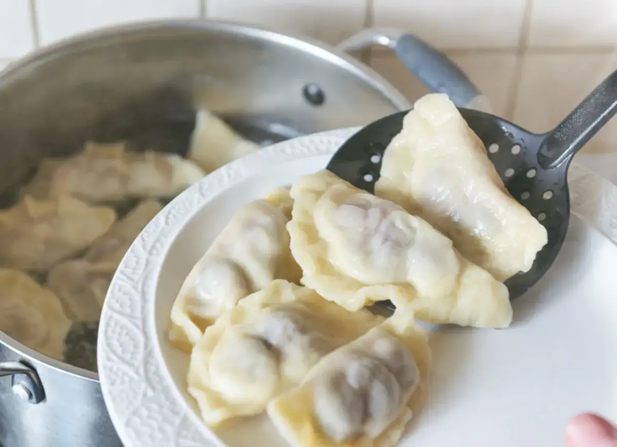 Gotowanie pierogów: wyjmowanie gotowych z garnka na talerz. Widać, ile gotować pierogi, by były idealne.