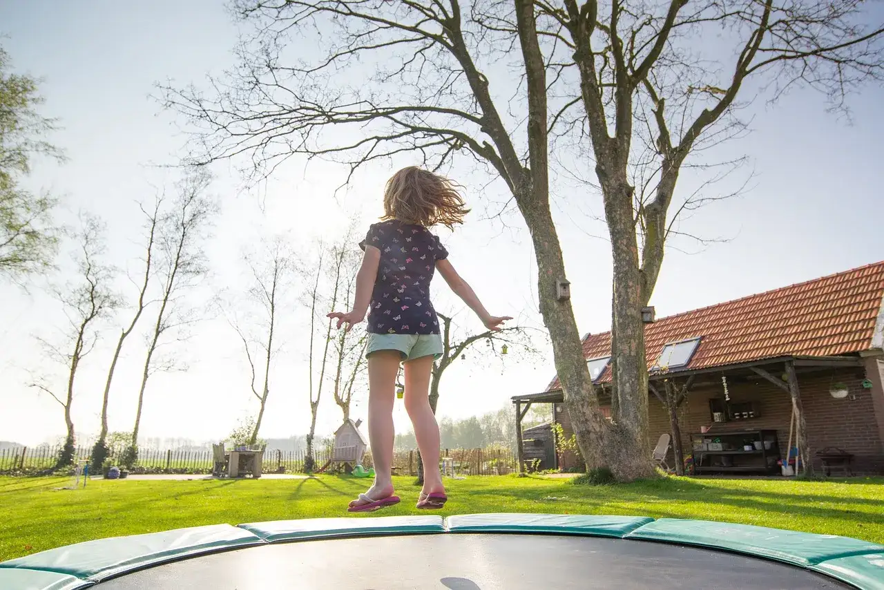 Dziewczynka skacze na trampolinie, ciesząc się ruchem i świeżym powietrzem. To świetna zabawa i aktywność fizyczna!