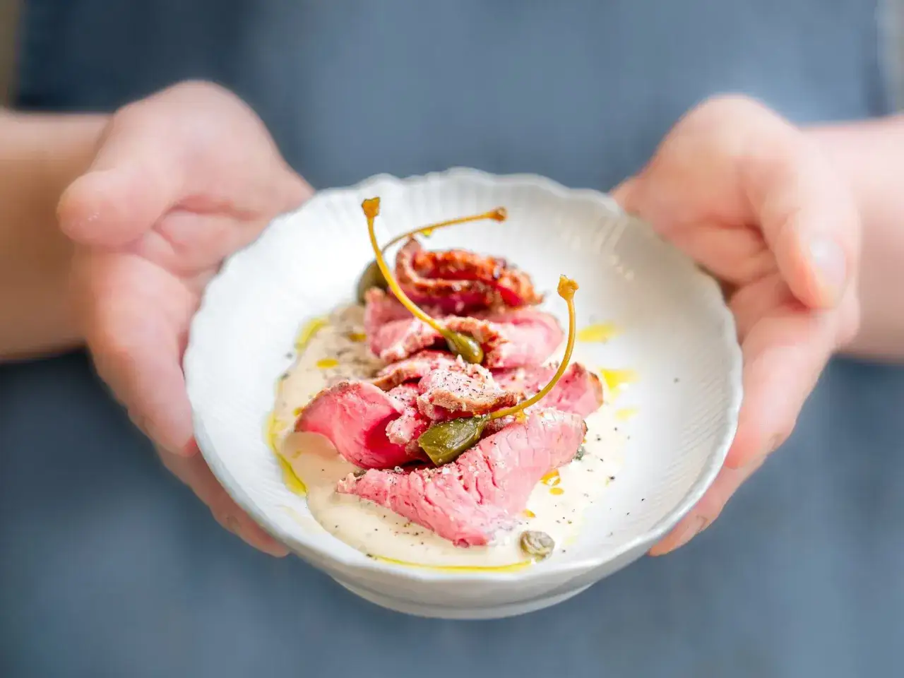 Fines tranches de vitello tonnato, napp&eacute;es d'une sauce cr&eacute;meuse et garnies de c&acirc;pres, pr&eacute;sent&eacute;es dans une assiette blanche.