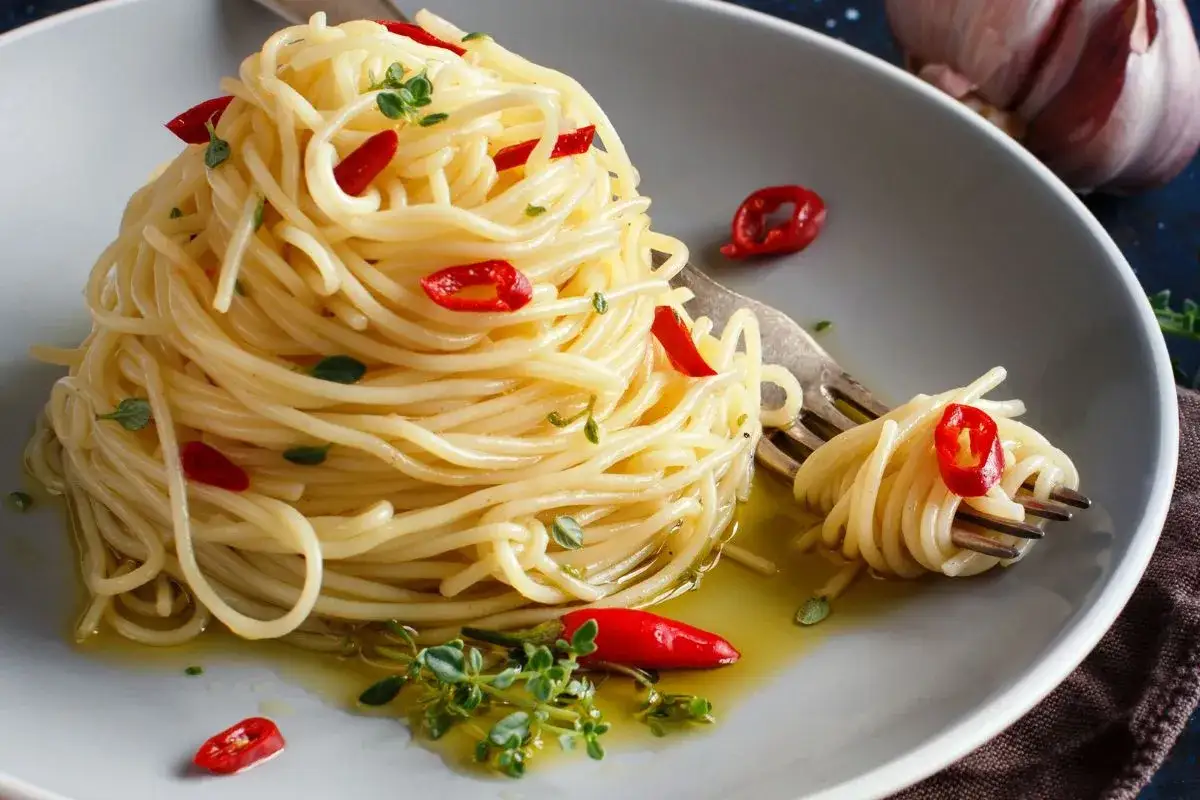 En portion aglio olio e peperoncino med spagetti, chili och örter på en grå tallrik.