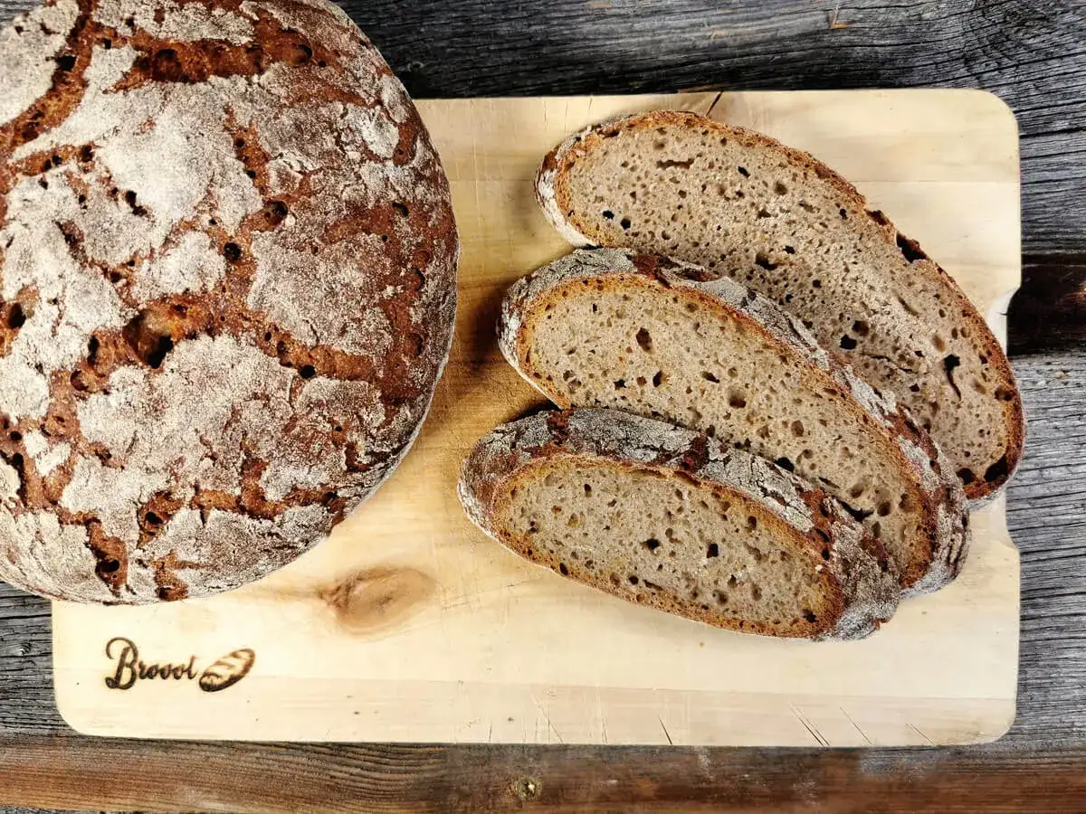 Ein rustikales, salzarmes Brot liegt neben frisch geschnittenen Scheiben auf einem Holzbrett.