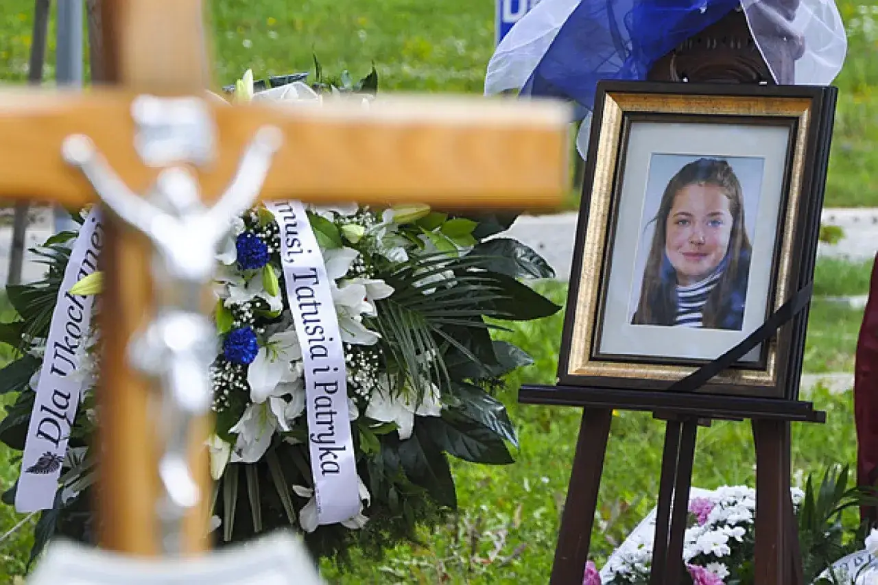 Portret uśmiechniętej Izabeli Strzałkowskiej obok krzyża i wieńca pogrzebowego.