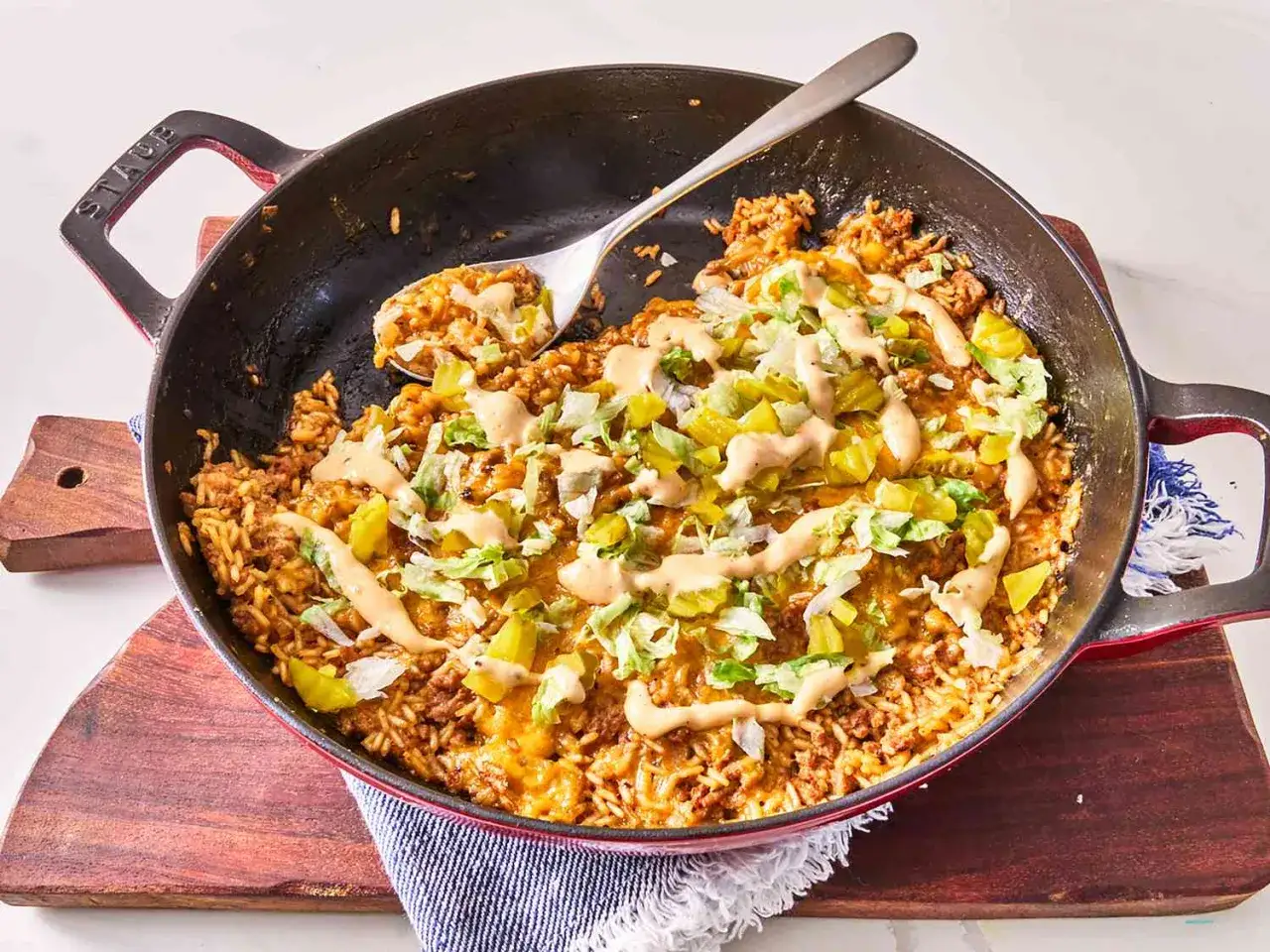 Herzhaftes Hackfleisch-Reis-Gericht in einer Pfanne, perfekt für schnelle Hackfleisch Rezepte. Mit Käse, Salat und Sauce garniert.