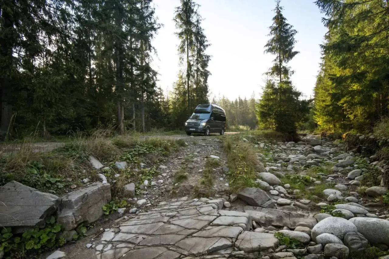 Ciemny kamper na leśnej drodze, kamieniste koryto strumienia obok. Idealne miejsce na caravaning na dziko.