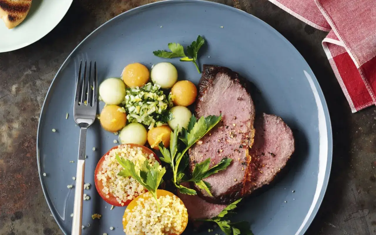 Tranches de rosbeef froid, accompagnées de billes de melon, de tomates farcies au quinoa et de persil frais. Un plat léger et coloré.