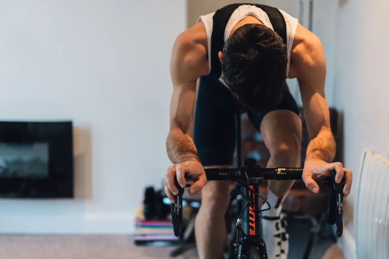 A cyclist intensely focused on a VO2 max workout, head down, arms gripping the handlebars.