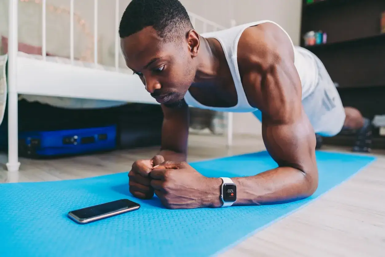Hombre haciendo plancha en casa, usando su reloj inteligente para seguir su rutina. ¡Perfecto para las mejores app ejercicio en casa gratis!