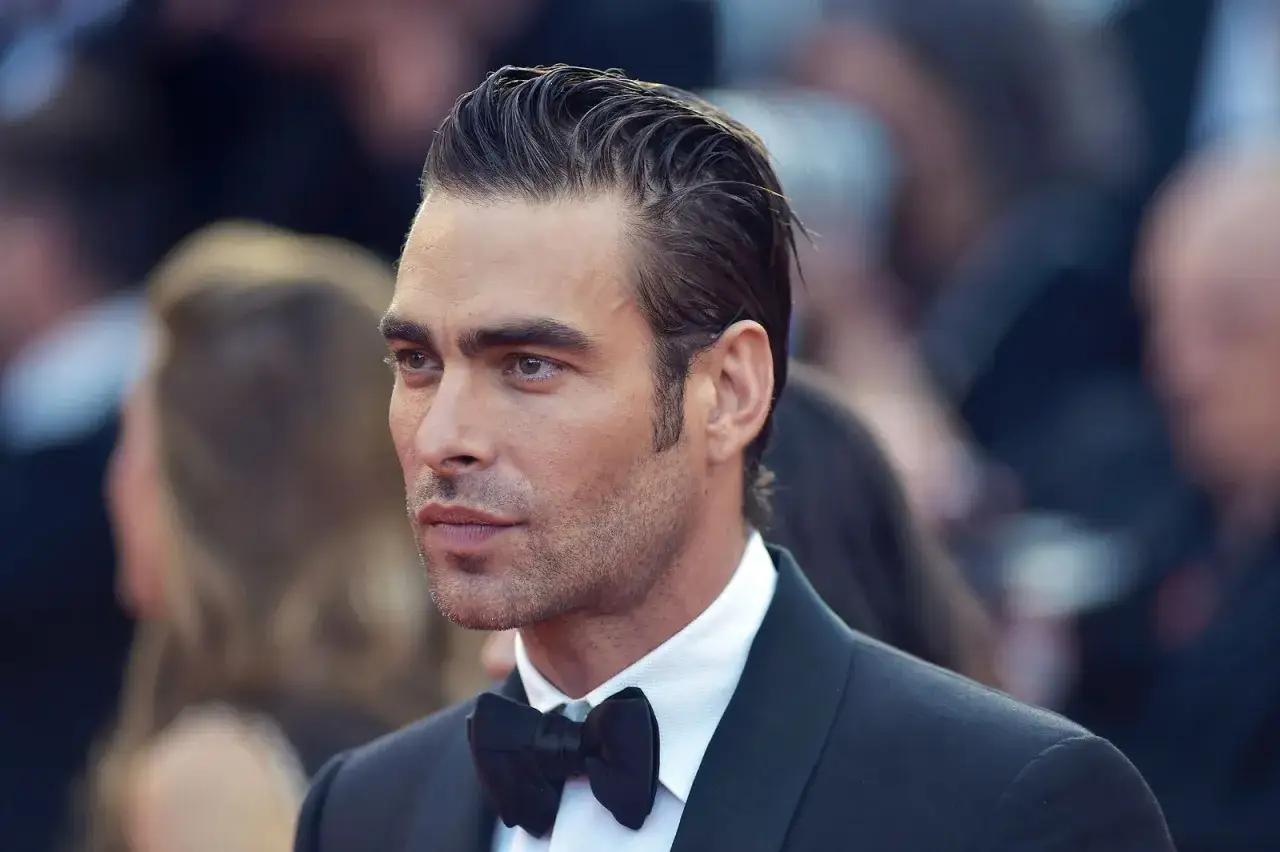 Hombre con un impecable corte de pelo old money, peinado hacia atr&aacute;s con gel, luciendo un esmoquin y pajarita negra.