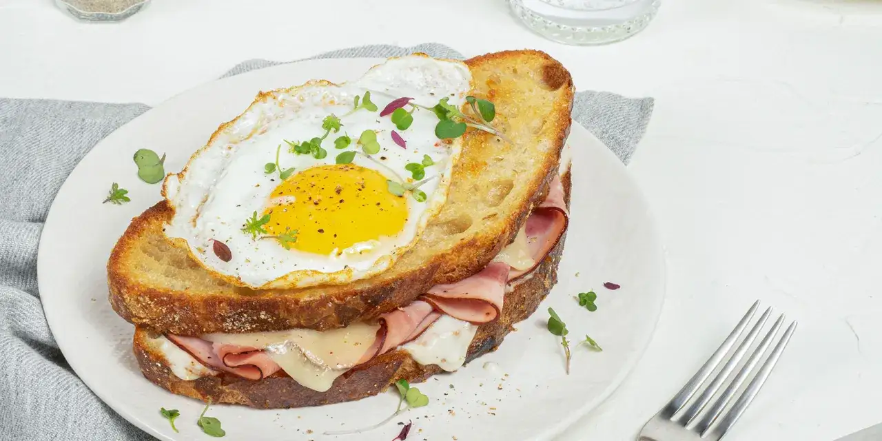 Un délicieux croque madame avec jambon, fromage fondant et un œuf au plat, garni de pousses fraîches.