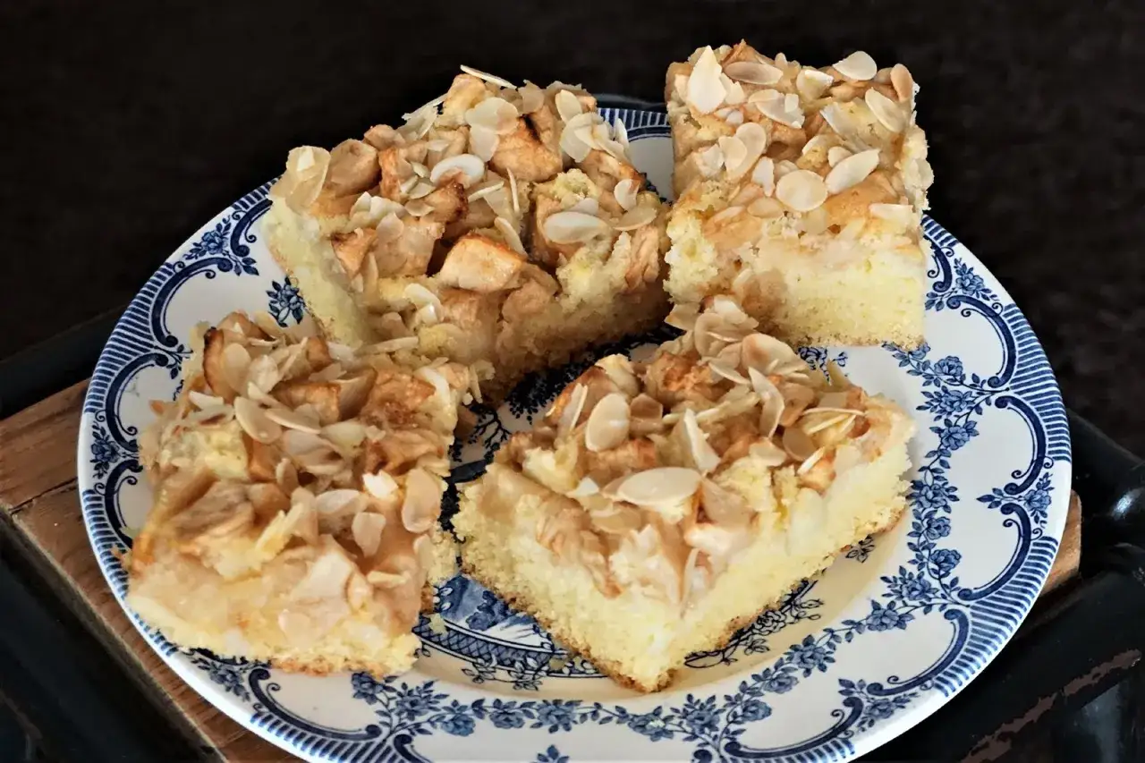 Vier St&uuml;cke saftiger Apfelkuchen mit Mandelkruste auf einem blau-wei&szlig;en Teller.
