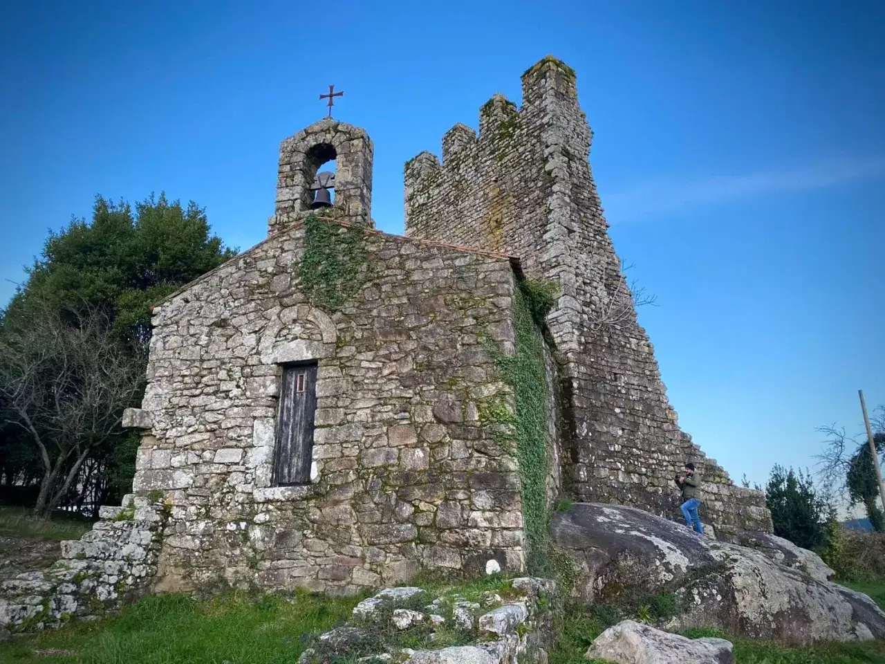 Antiguas torres de oeste de piedra, cubiertas de hiedra, con un campanario y un hombre fotografiando.