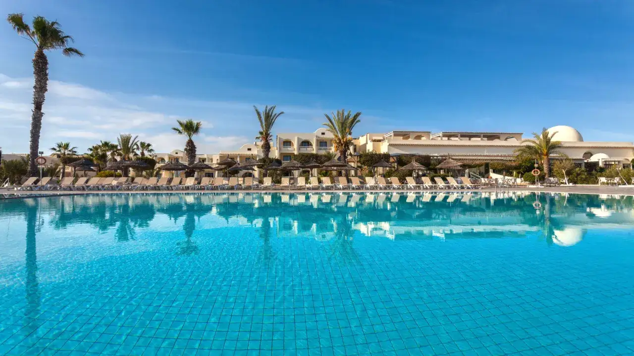 Basen w Djerba Aqua Resort (dawniej Sun Connect) z leżakami i palmami w tle.