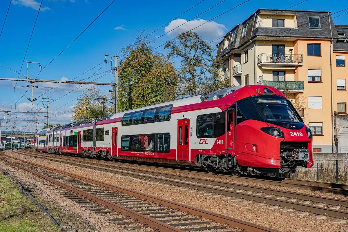 Czerwony pociąg CFL 2410, piętrowy, z białymi pasami, jedzie po torach. Ic co to za pociąg?