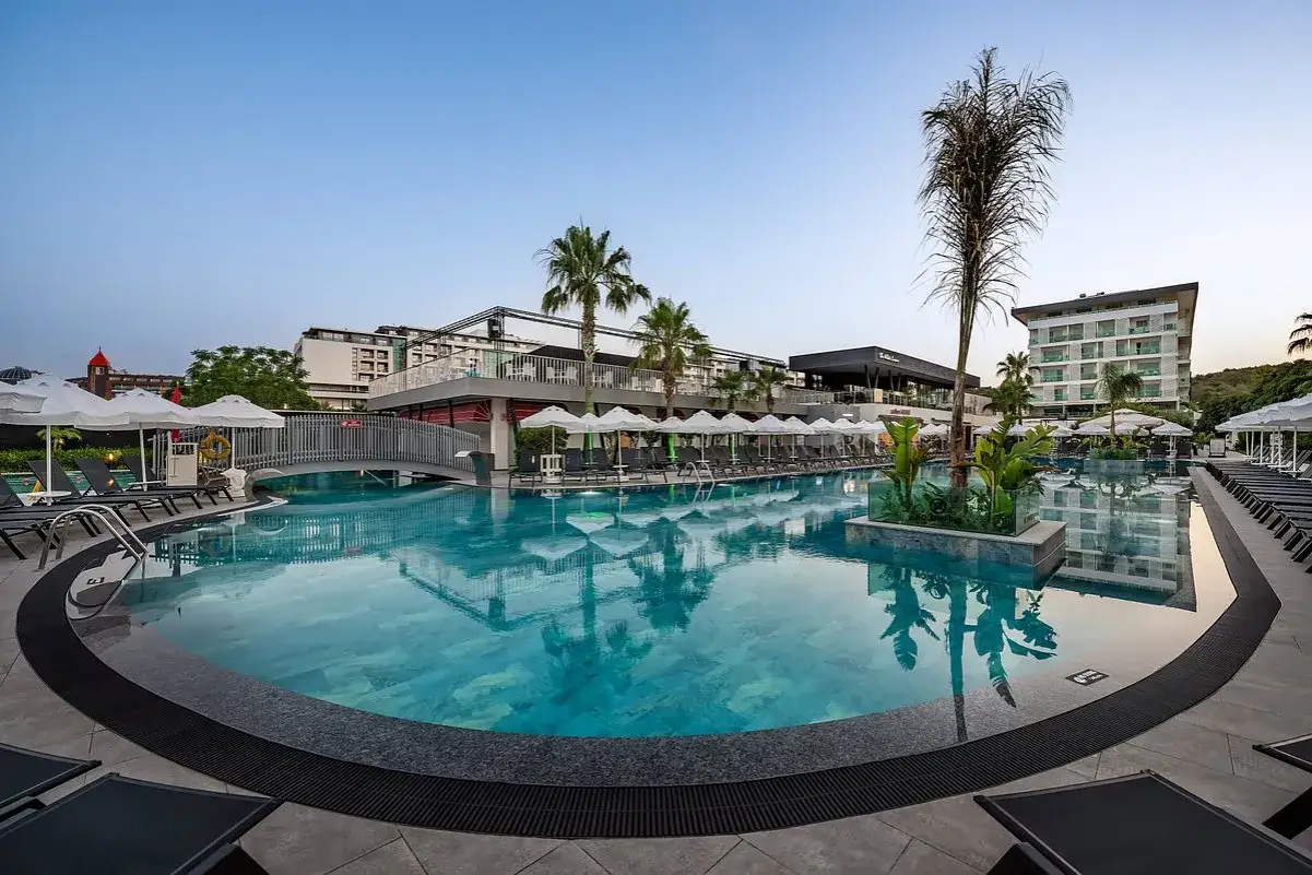 Einladender Poolbereich im quattro beach spa & resort mit Liegen, Sonnenschirmen und Palmen.