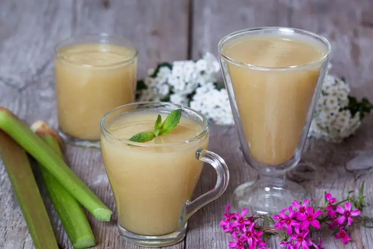 Trois verres de compote pomme rhubarbe, garnie de menthe, avec des tiges de rhubarbe et des fleurs roses et blanches.