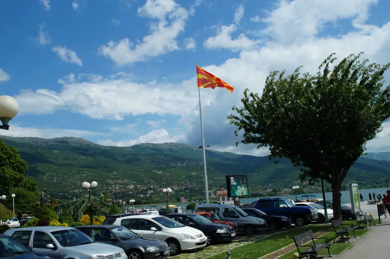 Autobus z Macedonii stoi na parkingu pod flagą narodową. W tle g&oacute;ry i jezioro.