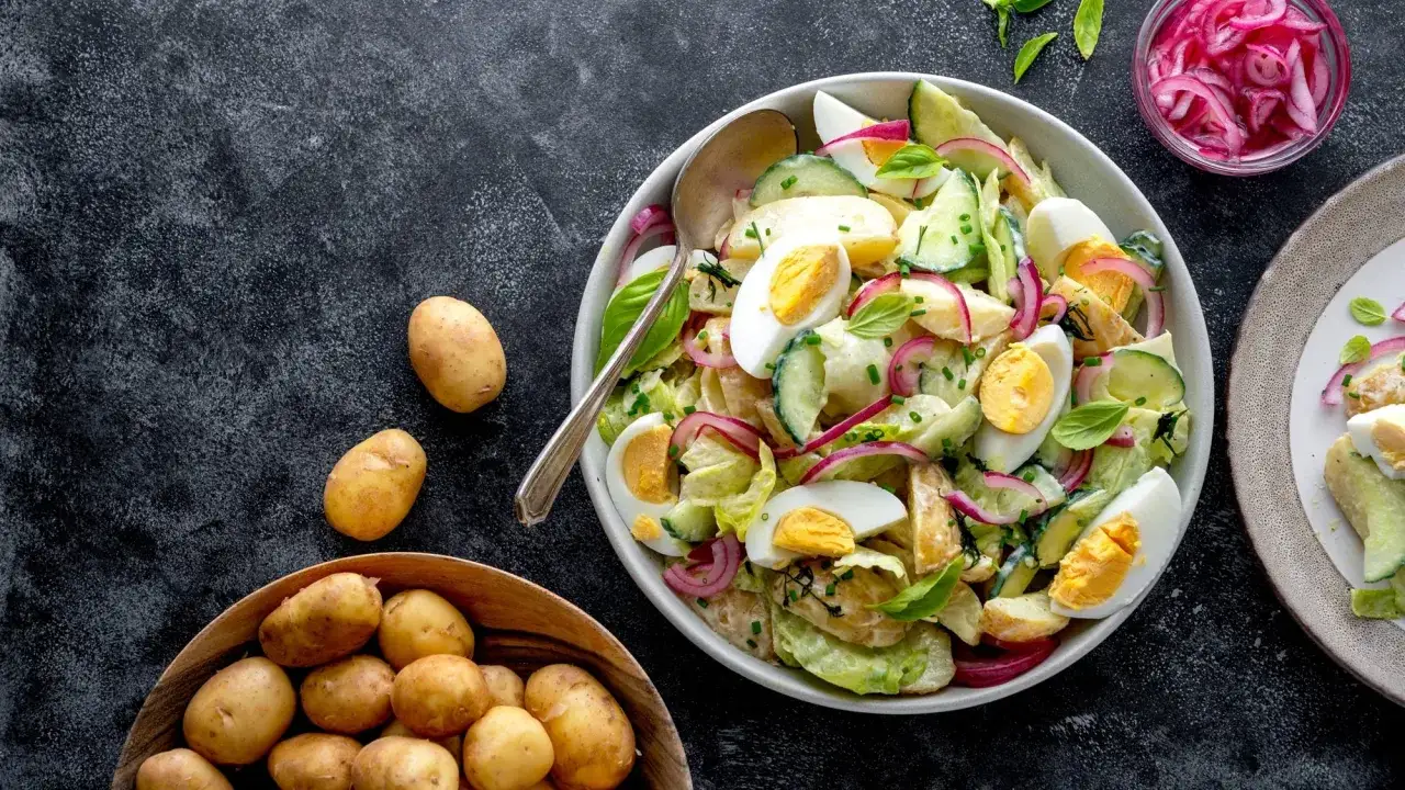 Herzhafter Kartoffelsalat mit Gurken, Eiern und roten Zwiebeln, garniert mit frischen Kräutern. Ein Klassiker, der immer schmeckt.