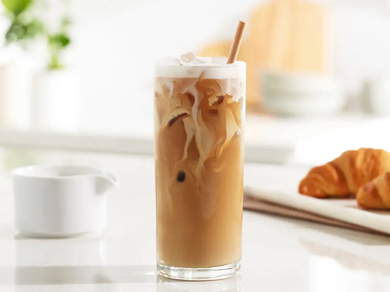 Orzeźwiające mrożone latte z mleczną pianką i słomką, obok dwa croissanty. Idealne na letnie popołudnie.