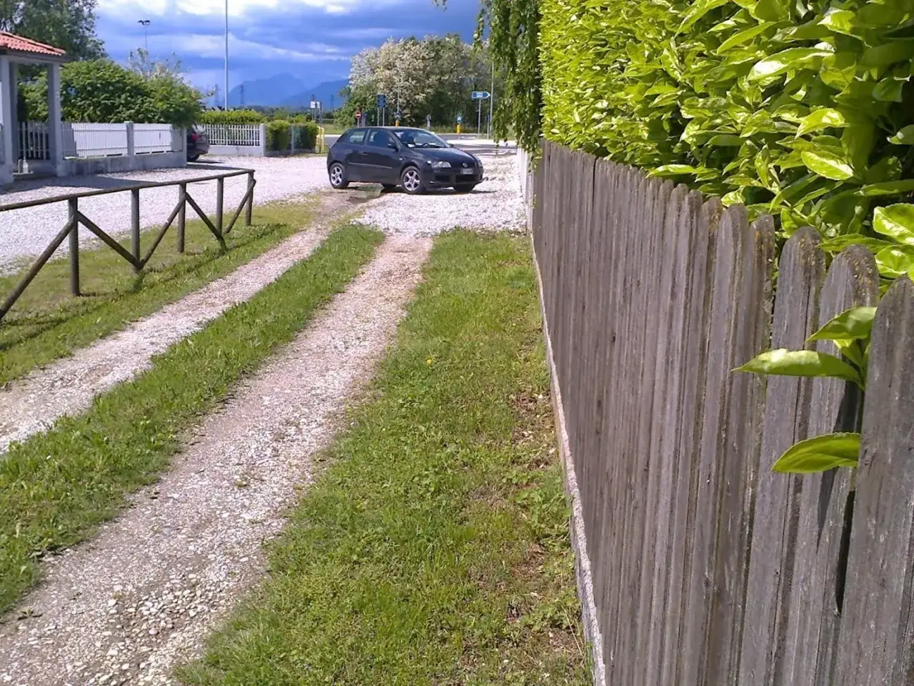 Strada sterrata con un'auto parcheggiata, delimitata da una staccionata in legno e siepe. Si intuisce il diritto di passaggio su strada privata.
