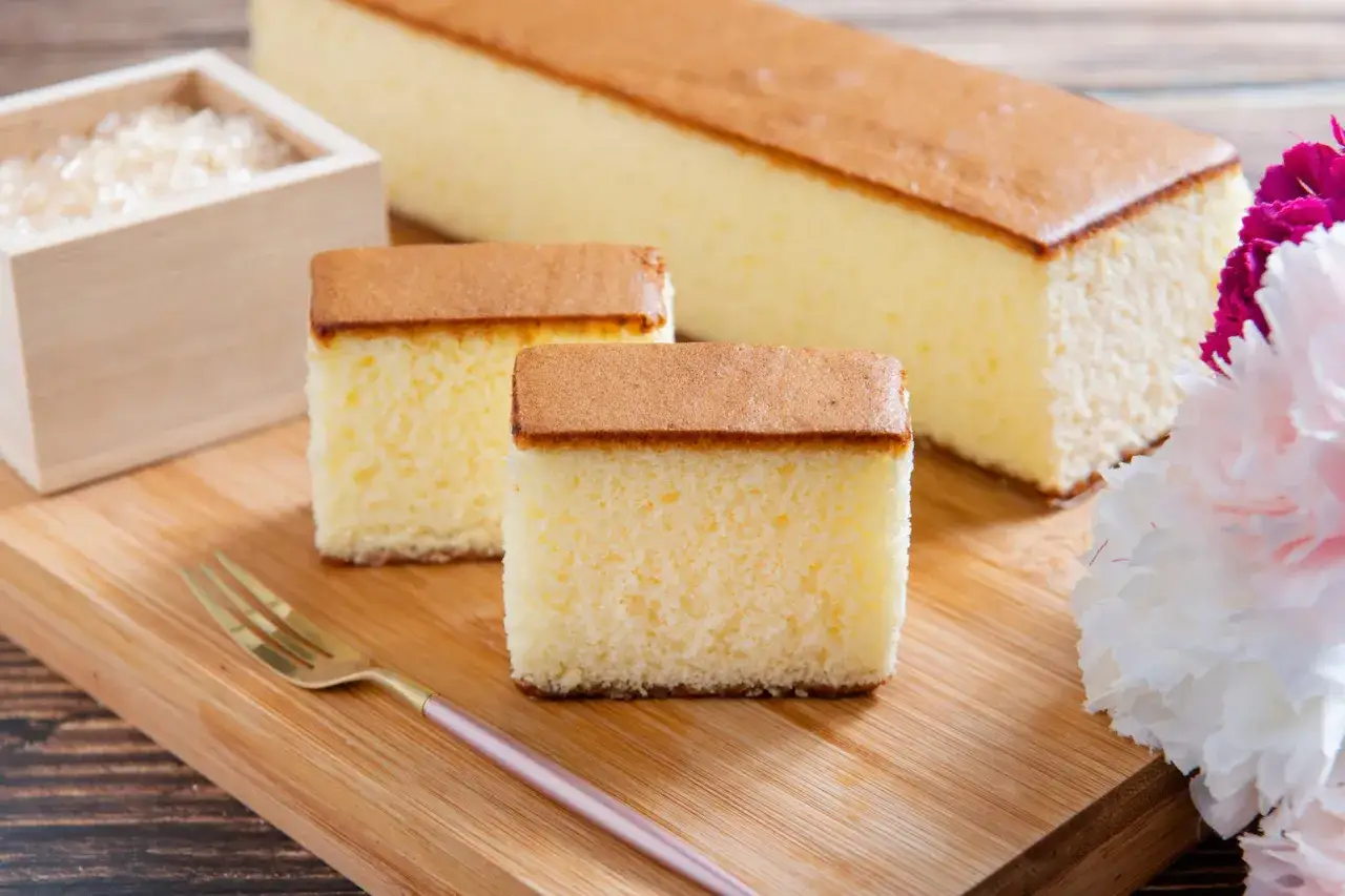 D&eacute;licieux gateau japonais, moelleux et a&eacute;rien, coup&eacute; en tranches sur une planche en bois, avec une petite fourchette dor&eacute;e et des fleurs.
