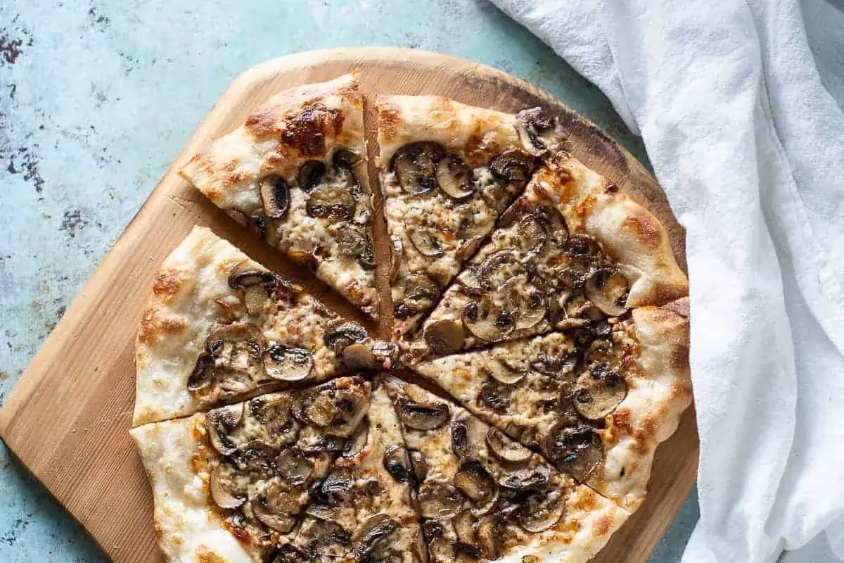 En skivad pizza de hongos med gyllene skorpa och rikligt med champinjoner, serverad p&aring; en tr&auml;sk&auml;rbr&auml;da.
