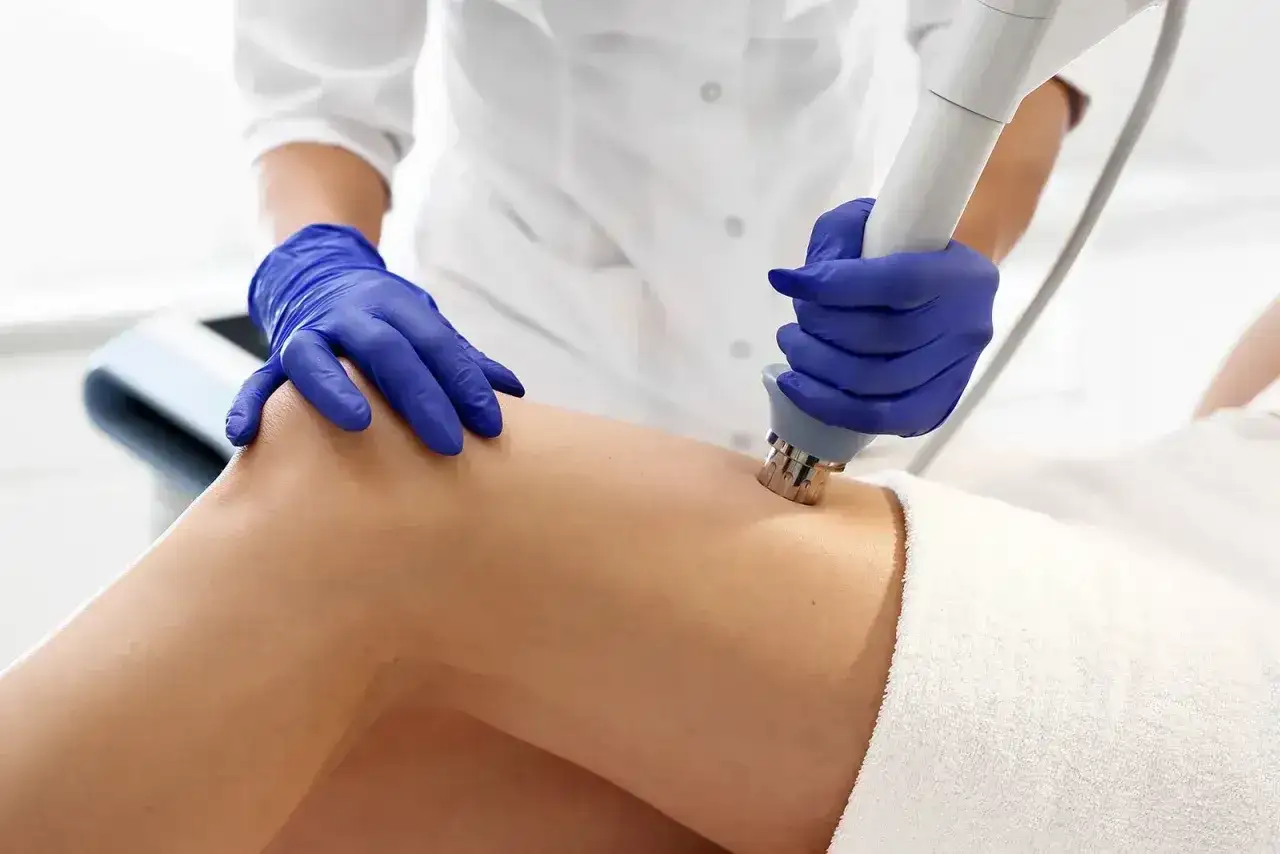 Fizjoterapeuta w niebieskich rękawiczkach wykonuje zabieg laserem na udzie pacjenta. Należy pamiętać o przeciwwskazaniach do fizykoterapii laserowej.