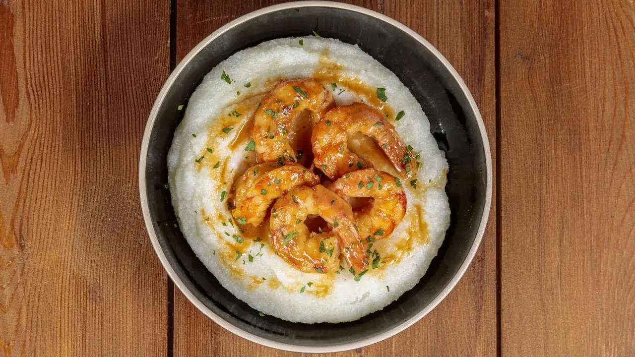 Gamberoni al guazzetto su un letto di polenta cremosa, guarniti con prezzemolo tritato. Un piatto invitante e saporito.
