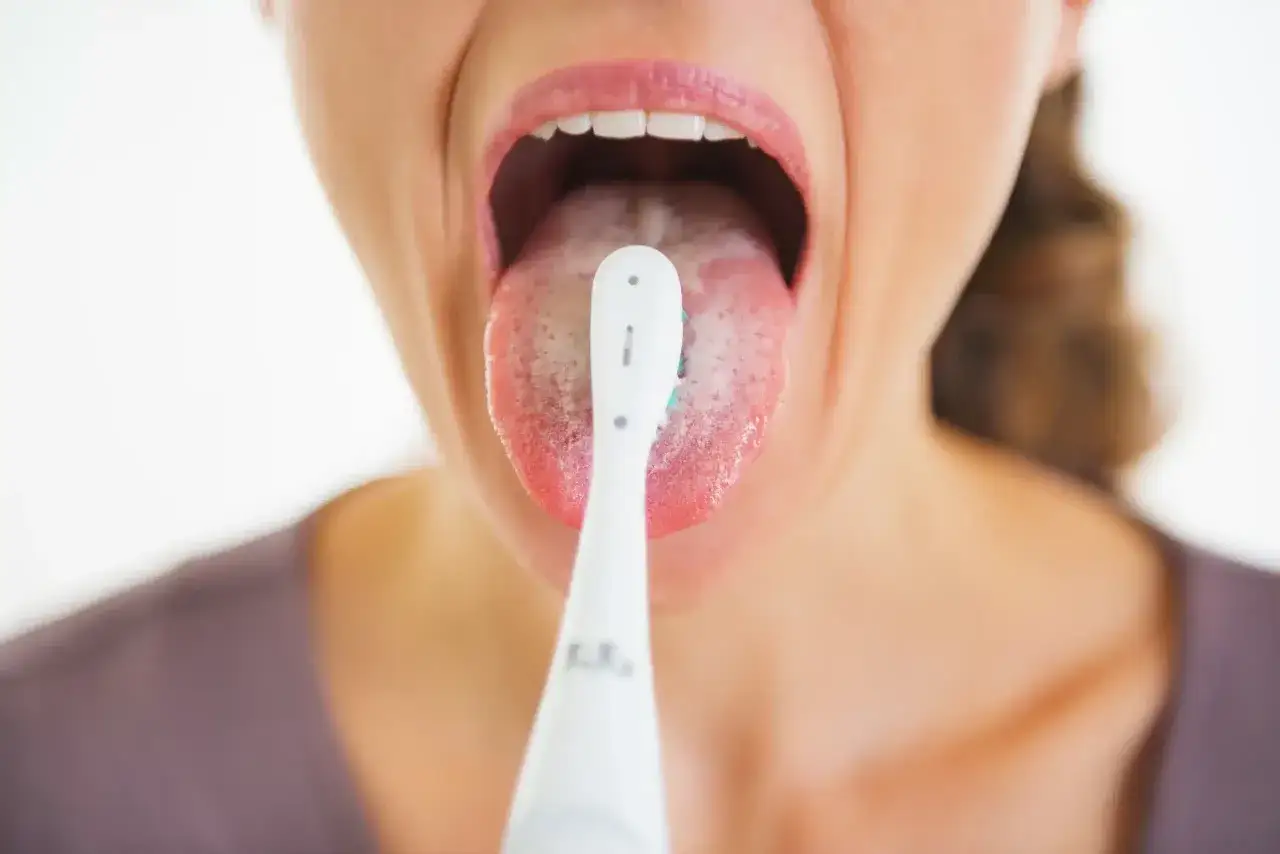 Persona cepillando su lengua blanxa con un cepillo el&eacute;ctrico para una higiene bucal completa.