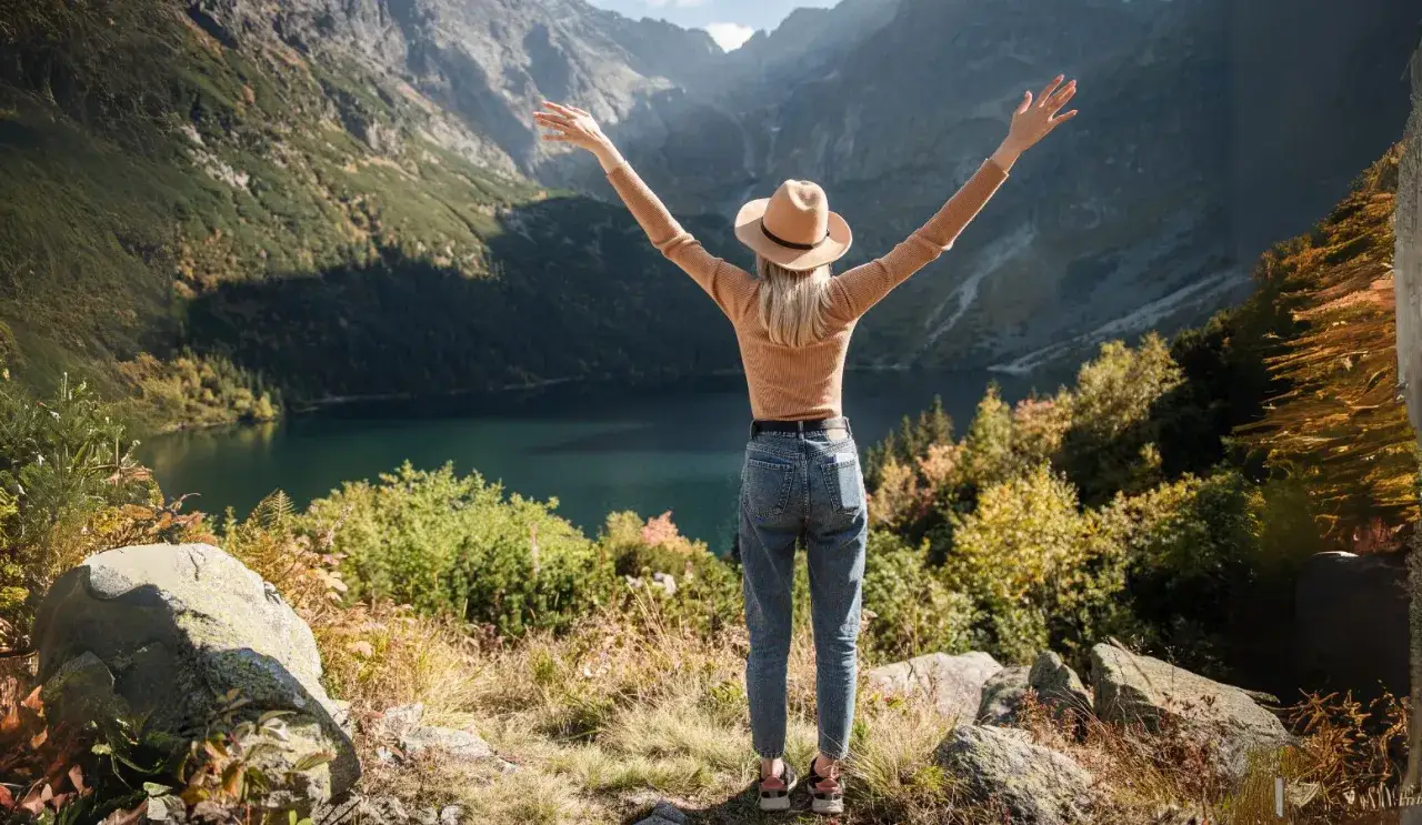 Mujer con brazos en alto admira un lago y monta&ntilde;as, un paisaje ideal para disfrutar de los Pirineos con ni&ntilde;os.